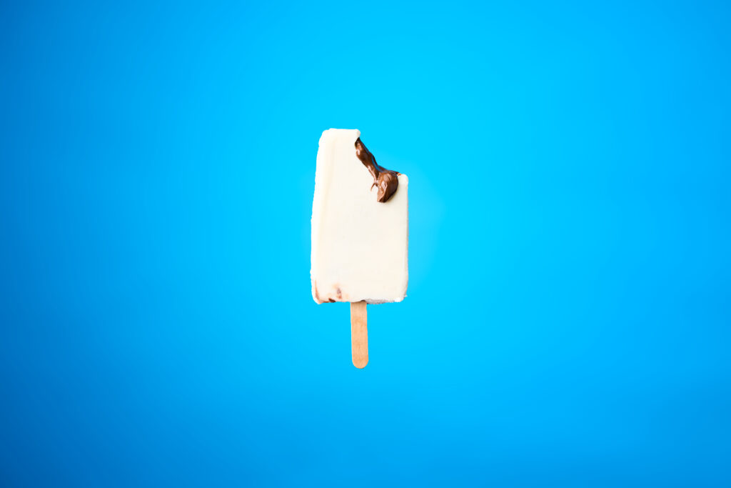 A banana and nutella filled popsicle with a bite taken from the right side is placed in front of a blue background