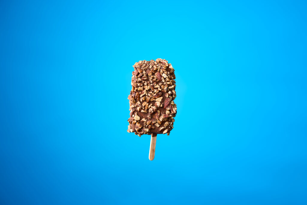 A popsicle dipped in chocolate and nuts is placed on a blue background